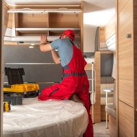 Caucasian RV Campers Technician in His 40s Performing Repairs Inside Modern Travel Trailer. Recreational Vehicles Maintenance.